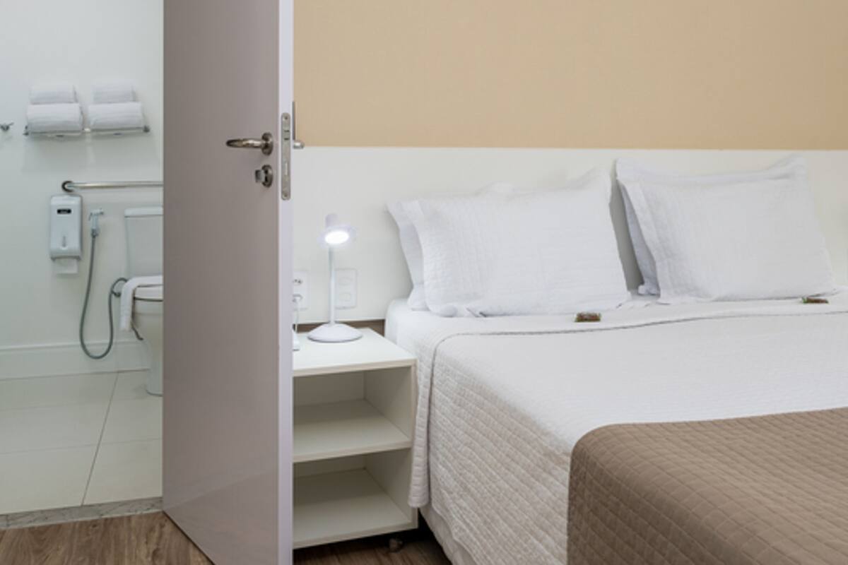 Ein Hotelzimmer mit Bett, Nachttisch mit Lampe, Dusche und Toilette.