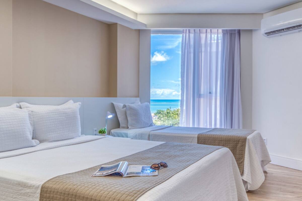 Ein modernes Hotelzimmer mit zwei Betten, einem großen Fenster mit Meerblick und einer Klimaanlage an der Wand.