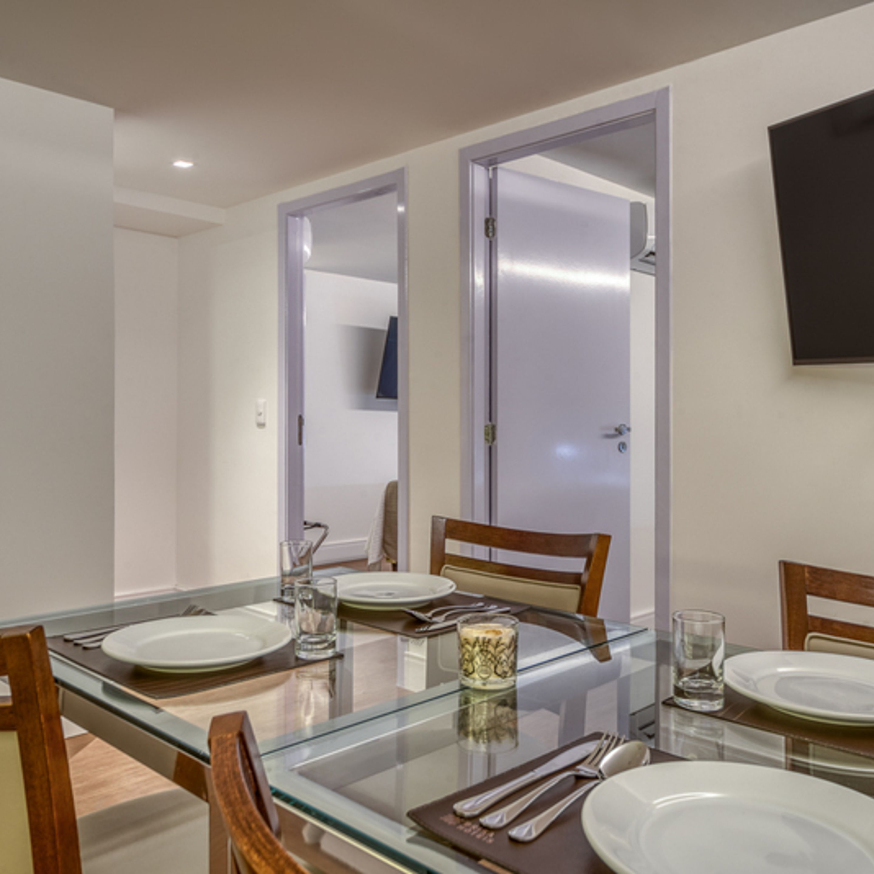 Un comedor con una mesa de vidrio, sillas y platos. Hay puertas que dan a otras habitaciones.