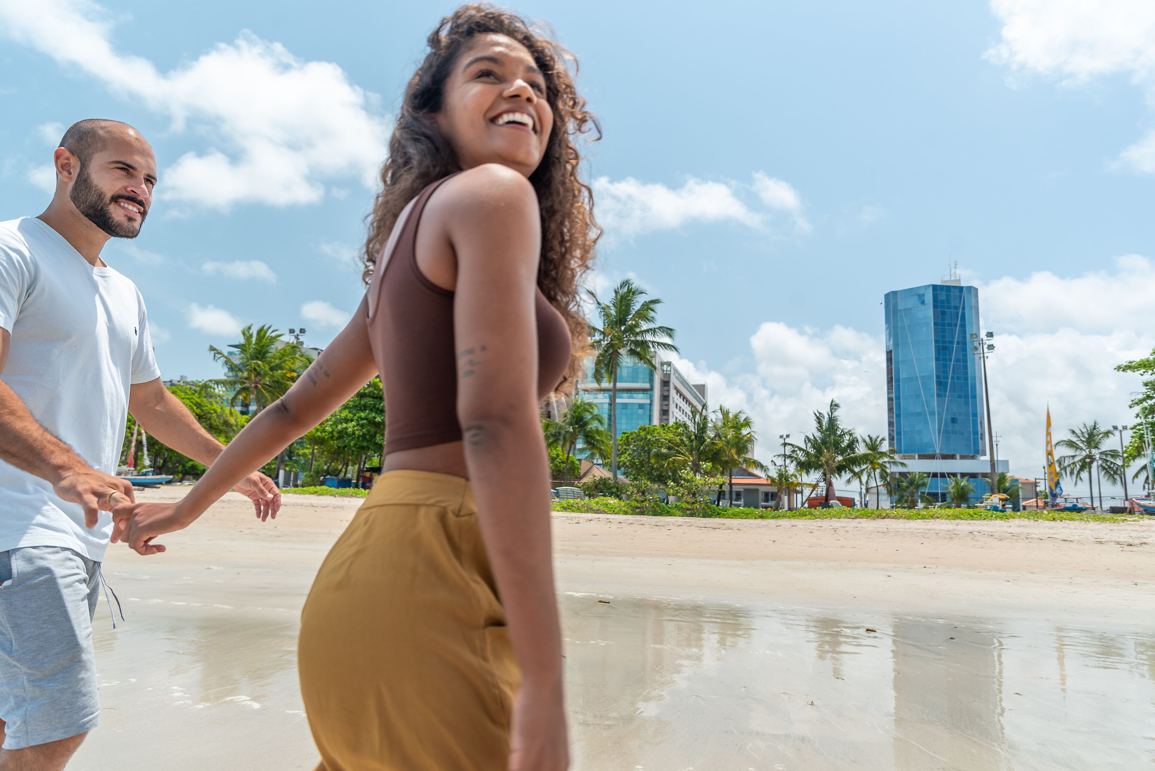 A couple walking on a beach with a modern building in the background.