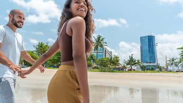 A couple walking on a beach with a modern building in the background.
