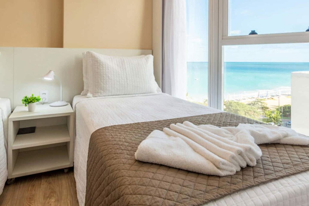 Una habitación de hotel con una cama, una mesita de noche, una lámpara y vistas a la playa.
