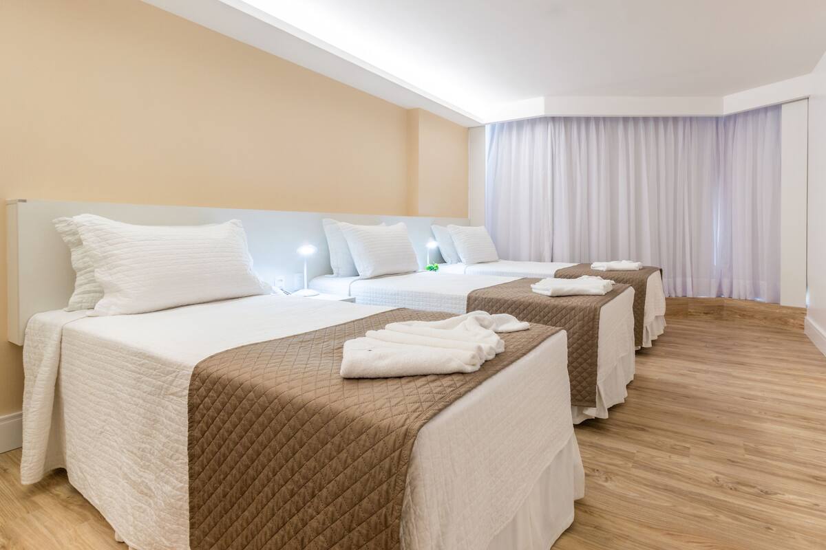 Ein Hotelzimmer mit drei Betten, jedes mit einem weißen Kopfteil und einer braunen gesteppten Bettdecke.