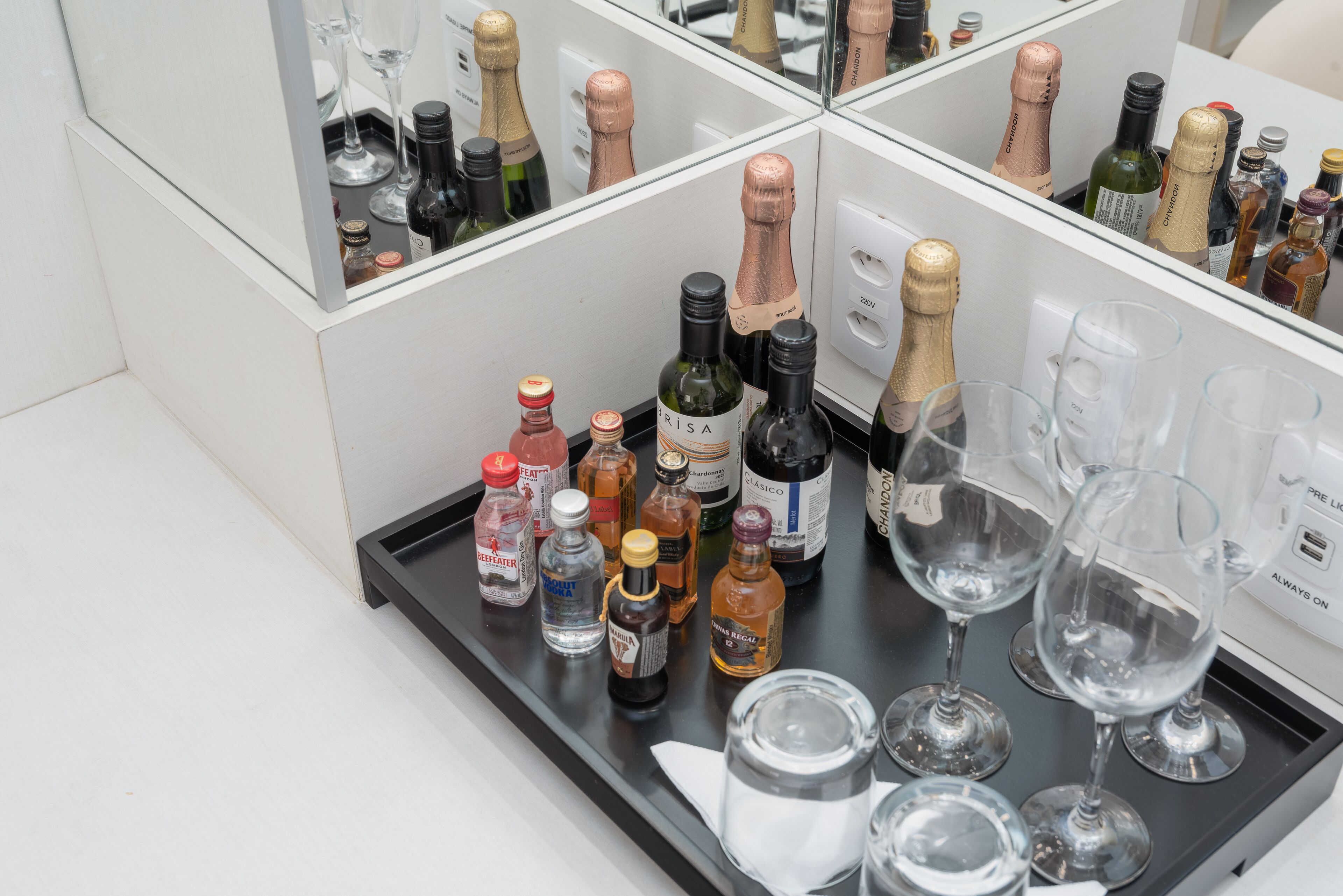 Una zona de bar con diferentes botellas y vasos, incluyendo champán y licores, sobre una bandeja negra.