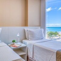 Una habitación de hotel con cama, escritorio con lámpara, una planta pequeña y vista a la playa.