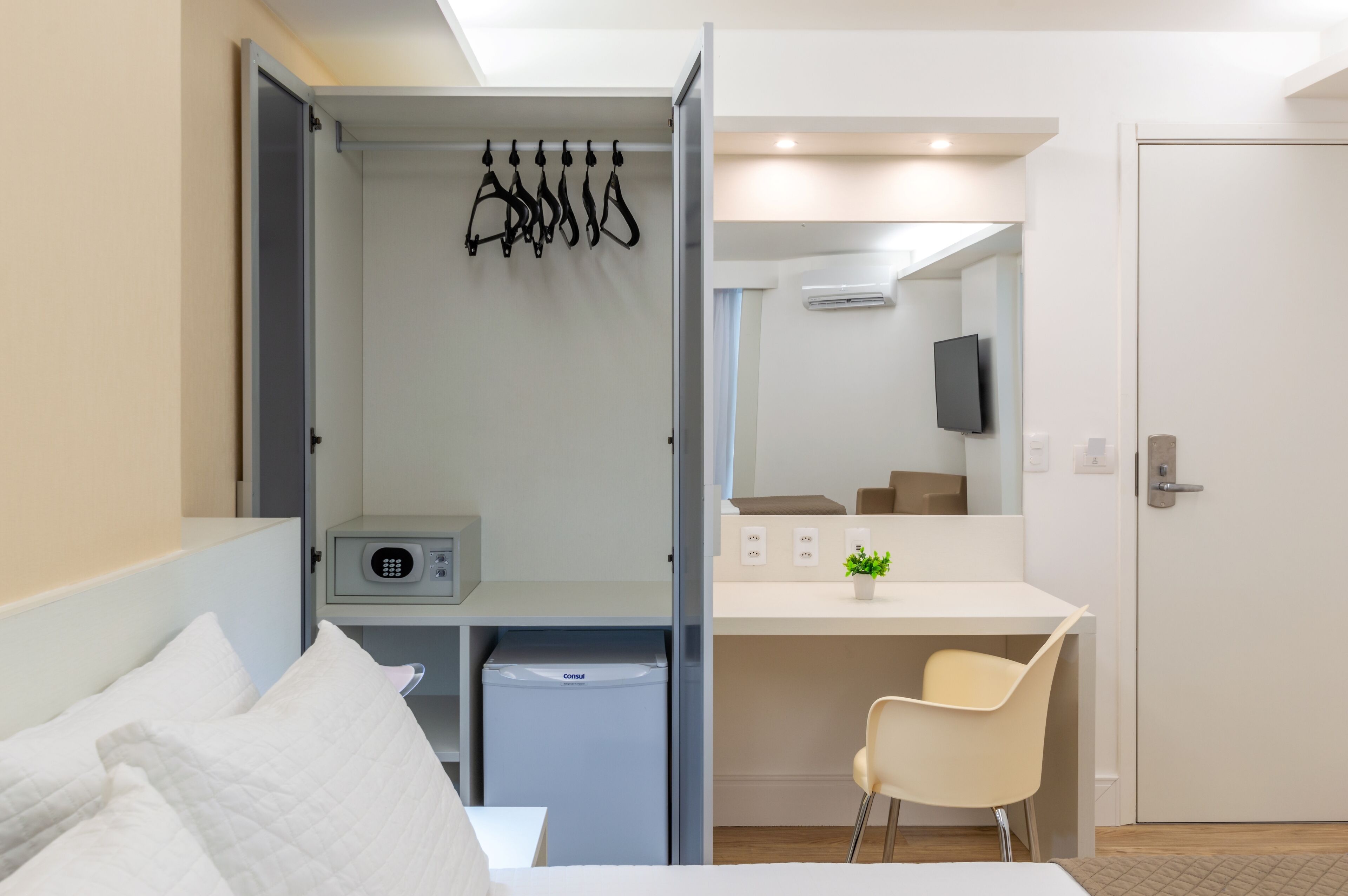 Una habitación de hotel moderna con cama, escritorio, silla, mini refrigerador, televisor y puerta.