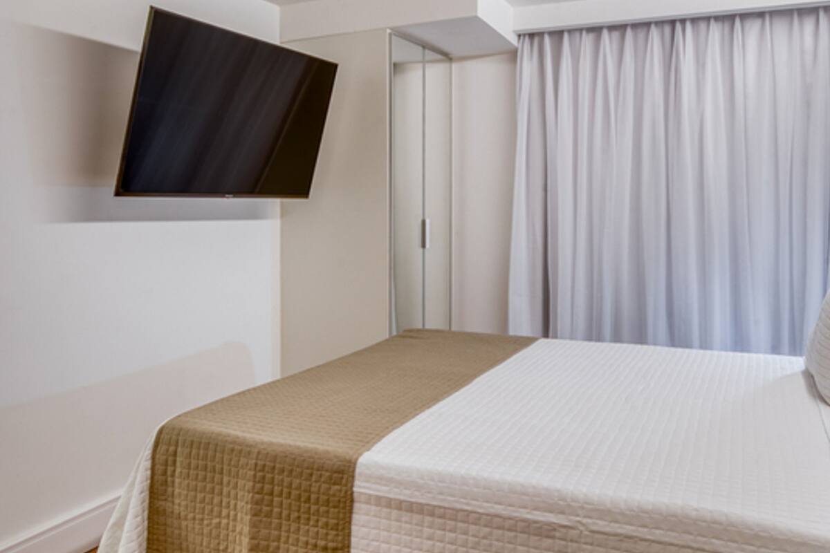 Ein Hotelzimmer mit Bett, einem an der Wand befestigten Flachbildfernseher und einem Fenster mit Vorhängen.