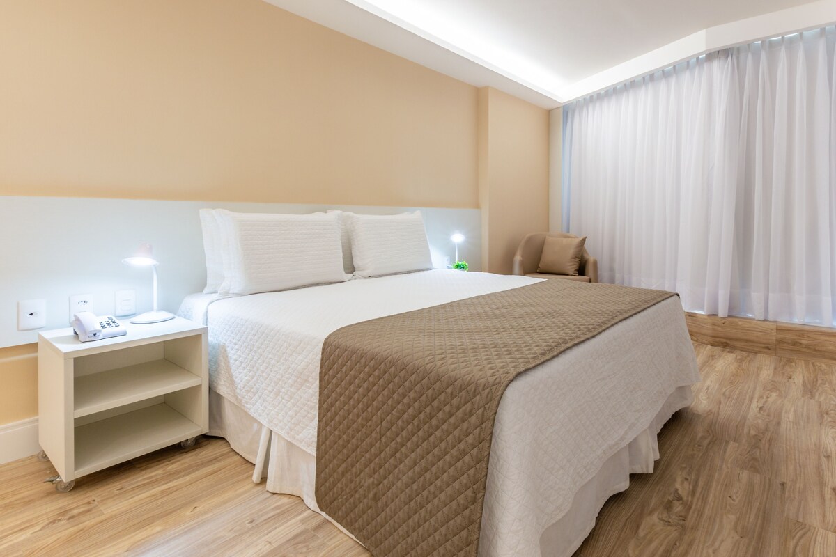 Una habitación de hotel con una cama, mesita de noche, lámpara y una silla.