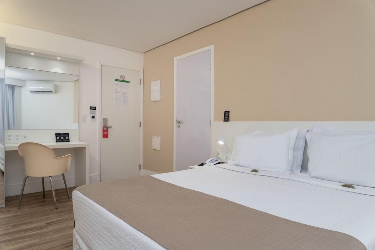 Una habitación de hotel con cama, escritorio, silla, espejo y puerta.