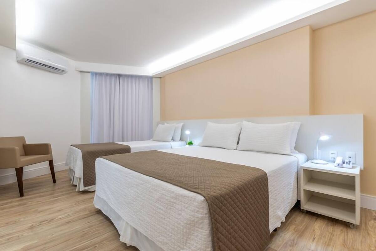 Ein Hotelzimmer mit zwei Betten, einem Sessel, einem Nachttisch mit Lampe und einer Klimaanlage.