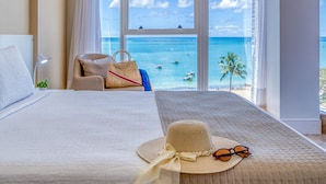 A hotel room with a large bed, a view of the ocean, and a beach visible through the window. - Hotel Brisa Suítes Pajuçara (Maceió)