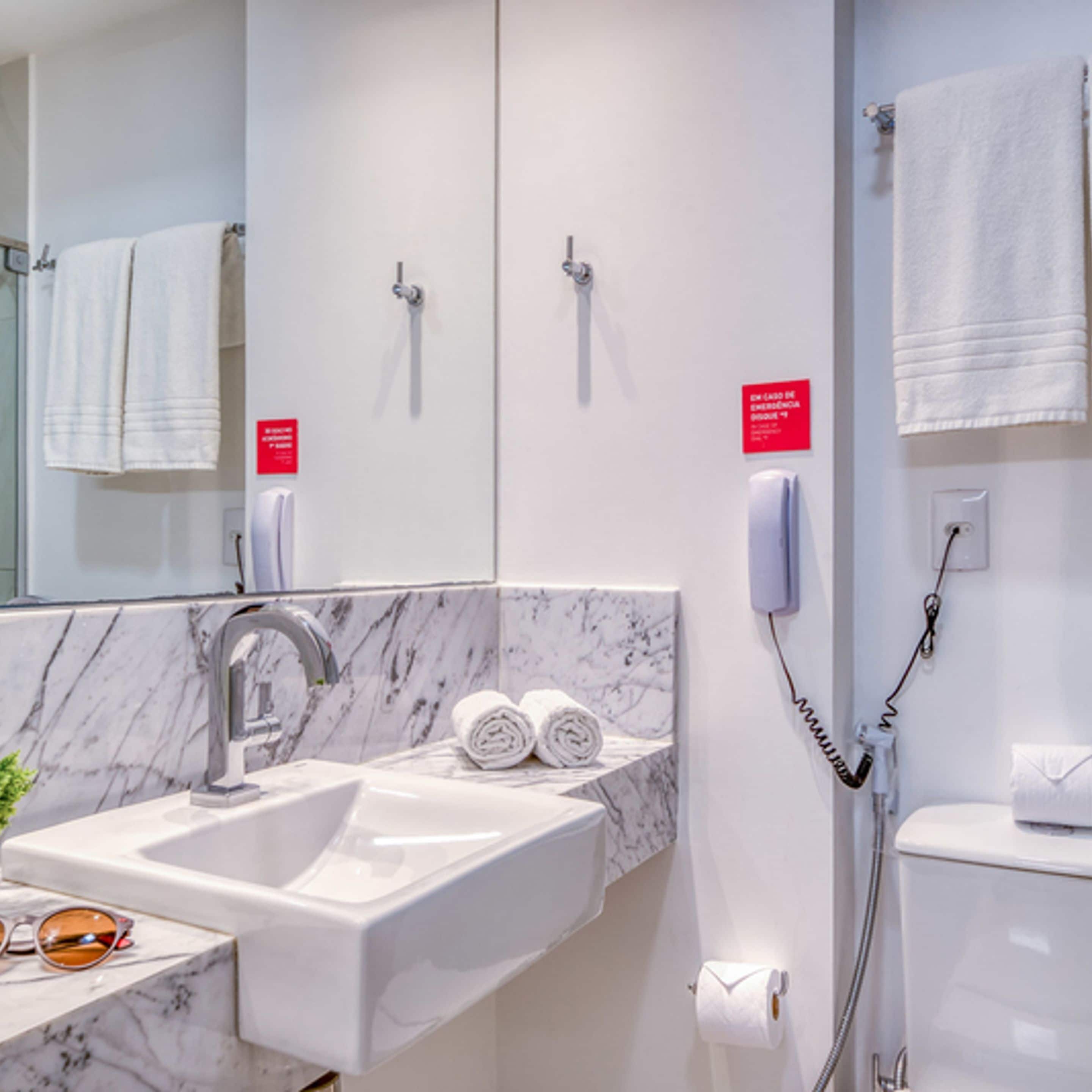 Un baño con lavamanos de mármol, espejo, toallero, inodoro y teléfono.