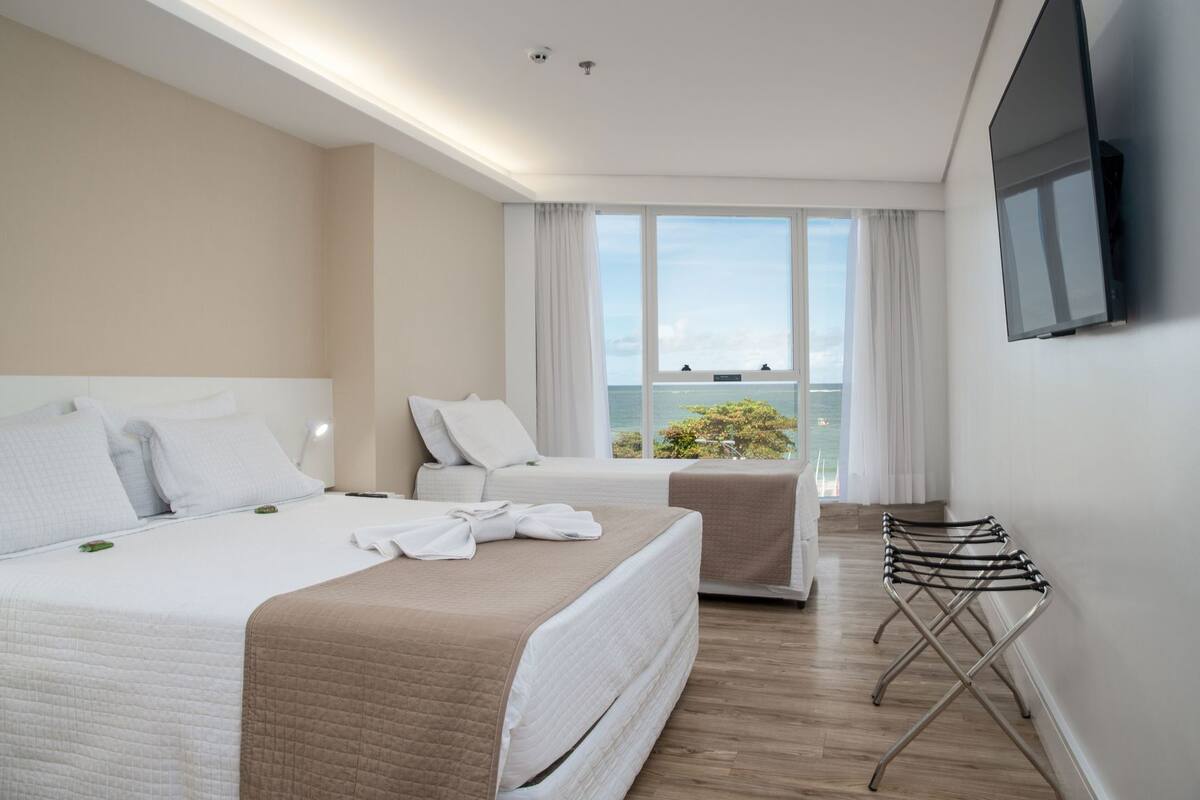 Ein Hotelzimmer mit zwei Betten, einem Fernseher, einem Balkon mit Aussicht und einem Wäscheständer.