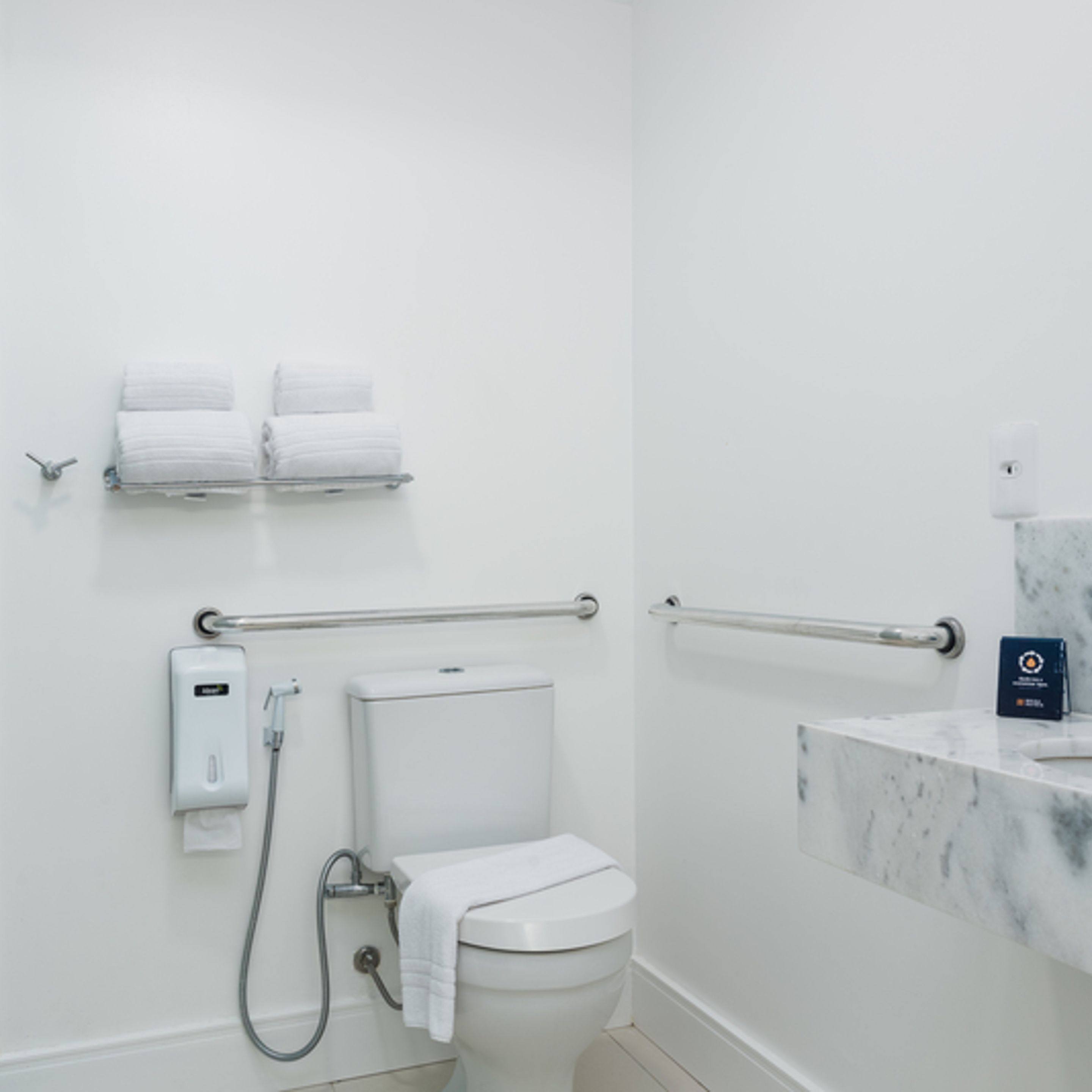 Un baño moderno con inodoro, barras de apoyo, secamanos y encimera de mármol.