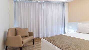Una habitación de hotel con cama, una silla, una mesita de noche y una ventana con cortinas.