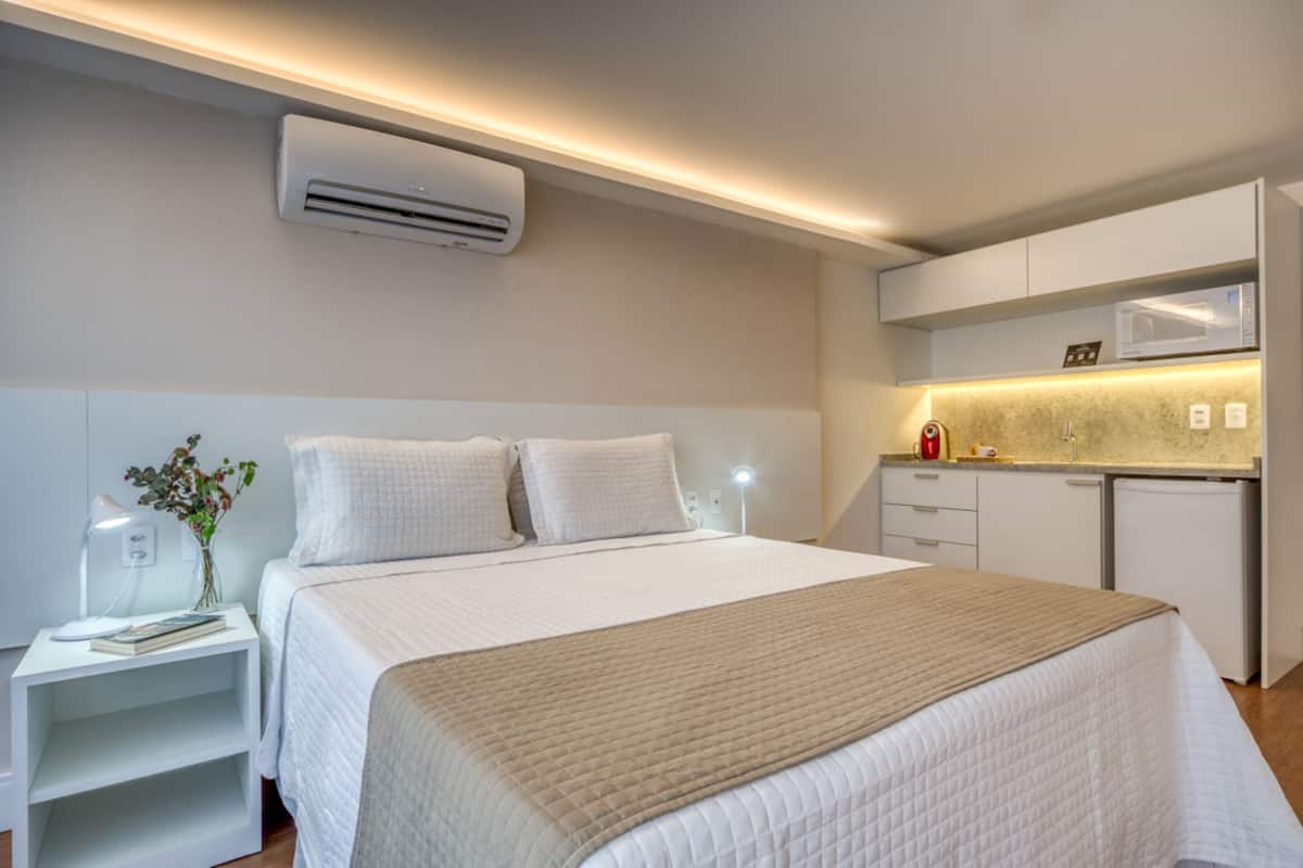 Ein modernes Hotelzimmer mit einem großen Bett, Nachttischen, einem kleinen Schreibtisch, einer Mikrowelle und einer Klimaanlage.