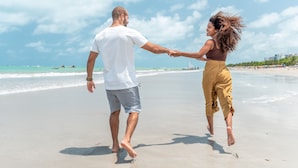 A couple walking hand in hand on a sandy beach with the ocean and a clear sky in the background. - Hotel Brisa Suítes Pajuçara (Maceió)