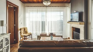 Ein Wohnzimmer mit Holzbalkendecke, einer Couch, einem Sessel, einem Tisch mit Dekoration, einem Fernseher und einem Kamin.