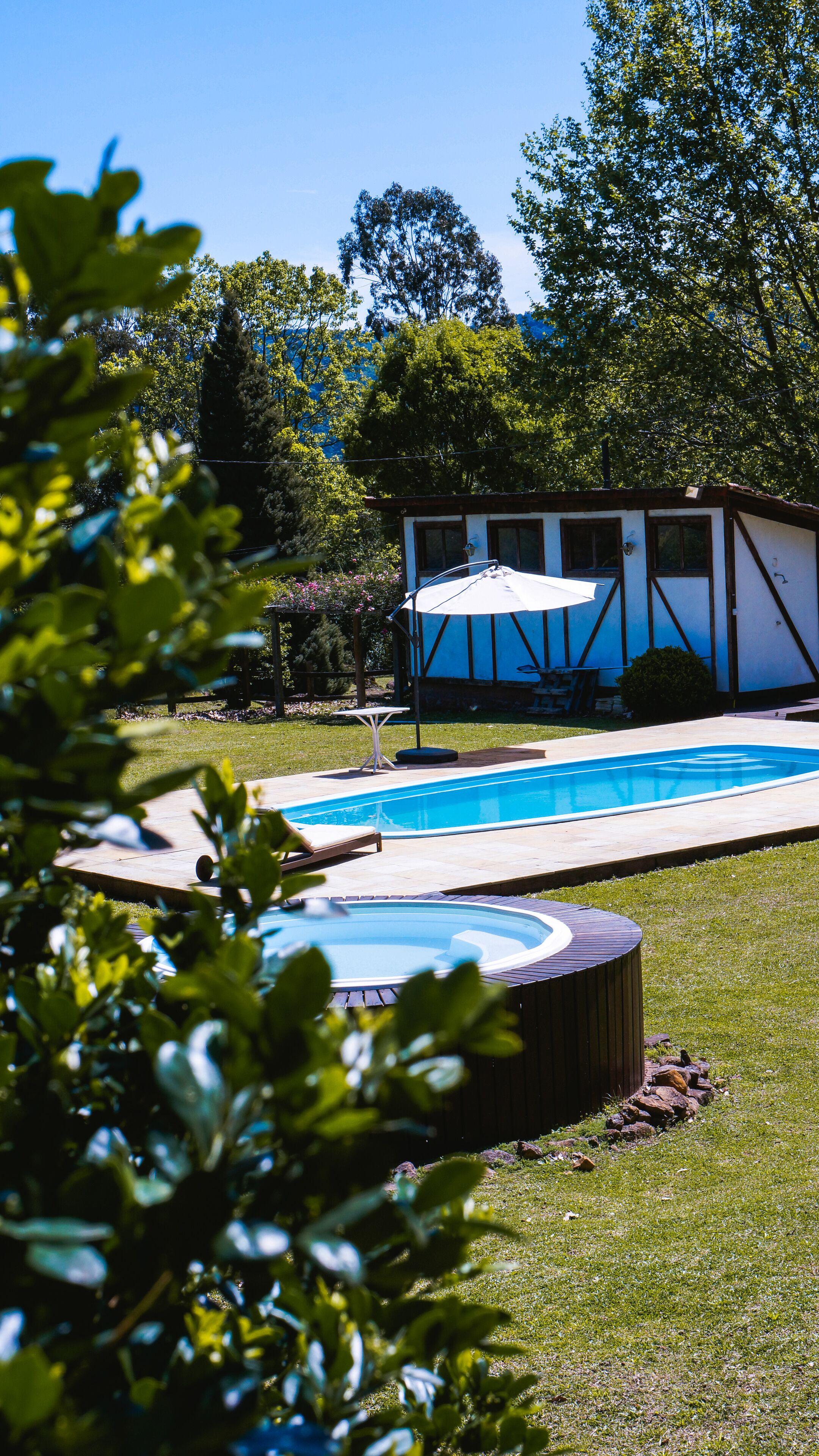 Una piscina con hidromasaje, un patio cubierto y un pequeño edificio en un jardín.