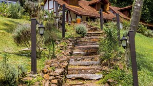 Ein gepflasterter Weg führt zu einem traditionellen Haus mit Ziegeldach, umgeben von üppiger Vegetation und Palmen.