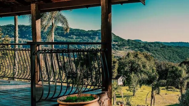 Eine Holzterrasse mit Metallgeländer, die über ein Tal mit üppiger Vegetation und Hügeln blickt.