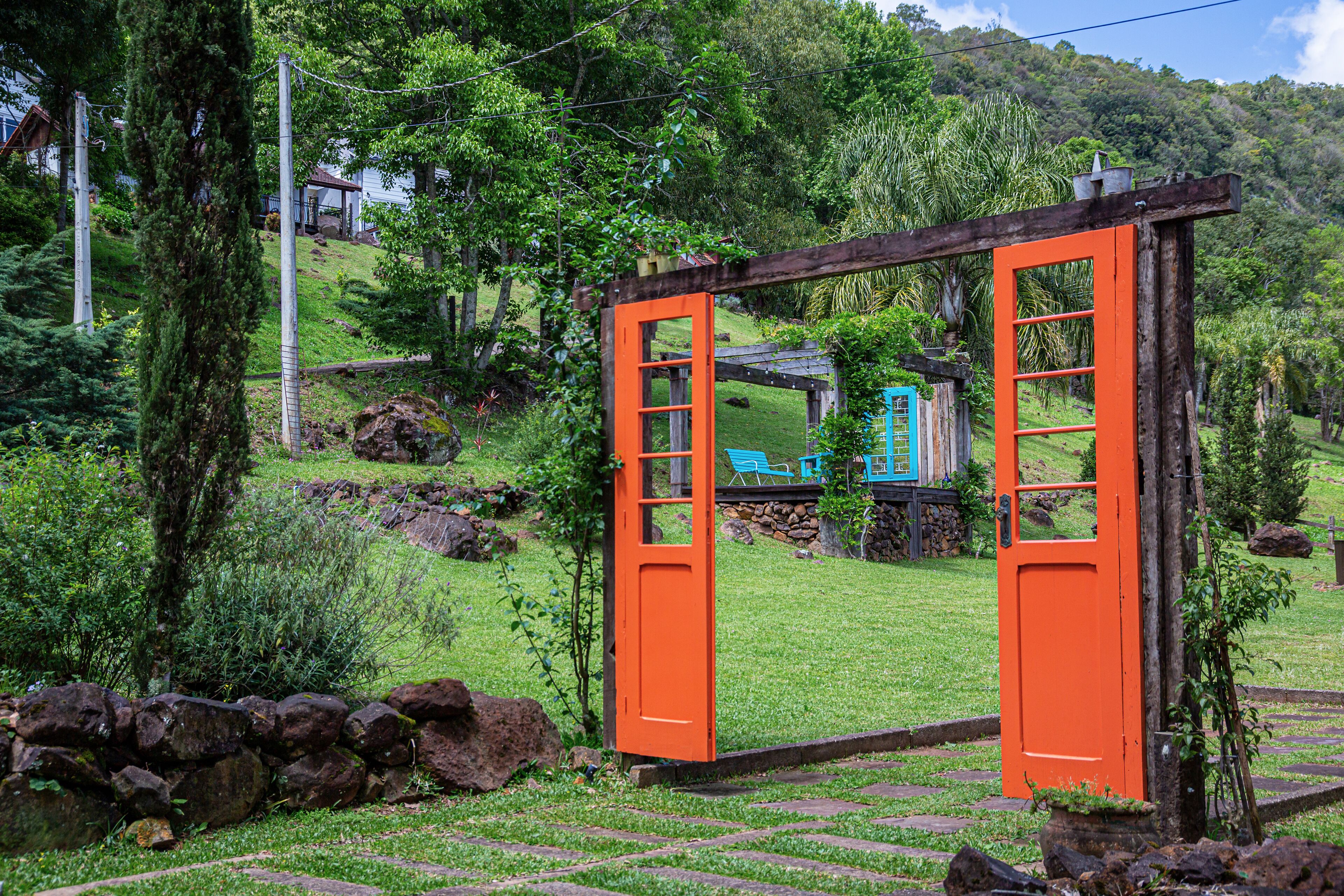 Una puerta naranja abierta que da a una estructura de juego azul en un entorno verde exuberante.