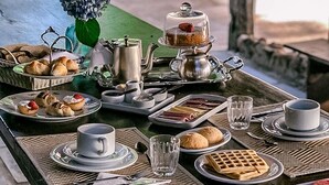 Ein Frühstückstisch im Freien mit verschiedenen Backwaren, Sandwiches und Getränken.