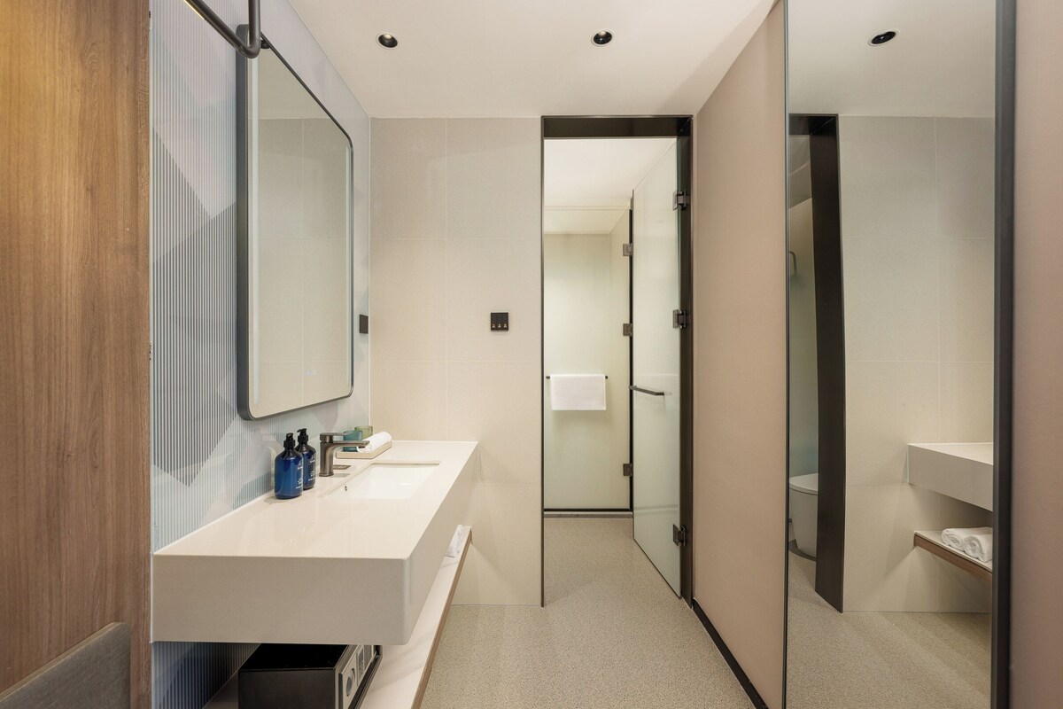 A modern bathroom with a large mirror, a white sink, and a glass shower enclosure.