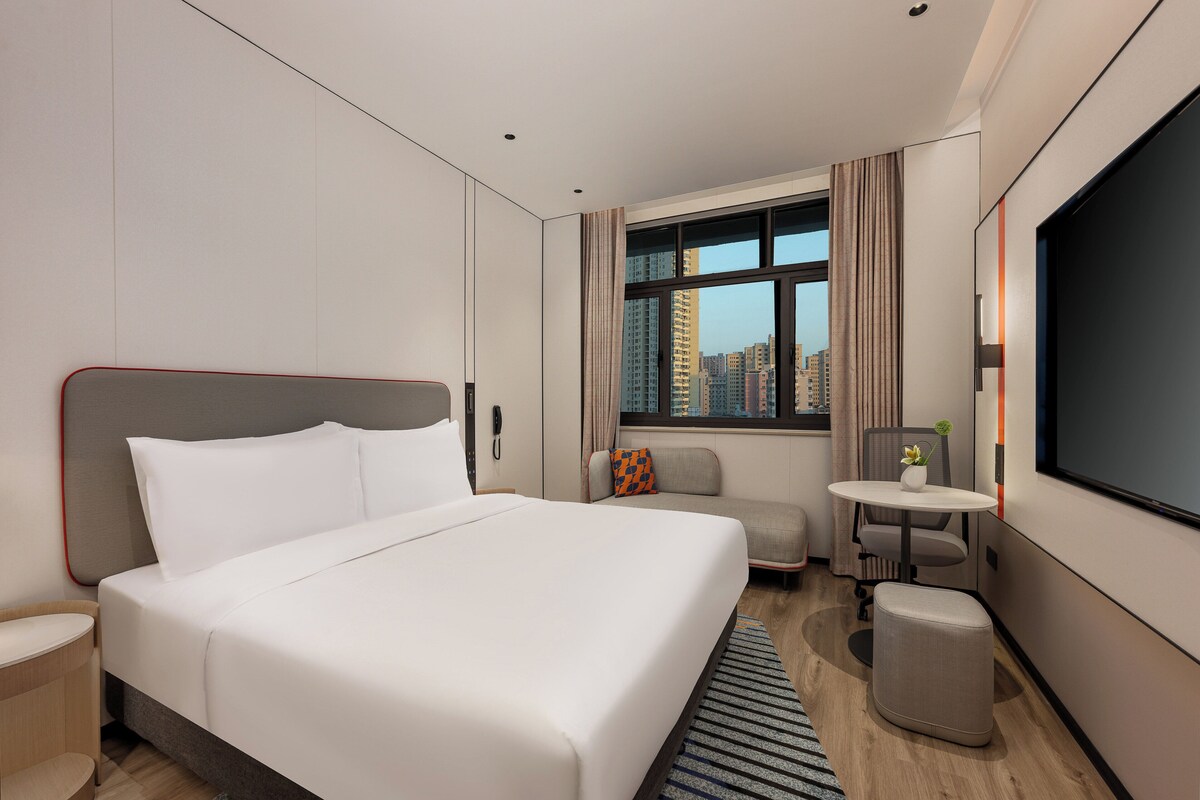 A modern hotel room with a large bed, a small sofa, a desk, and a TV.