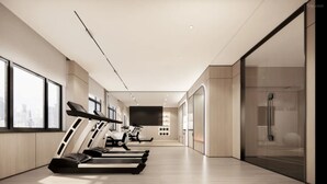 Un gimnasio moderno con cintas de correr, una pantalla de televisión y una zona de ducha de vidrio.