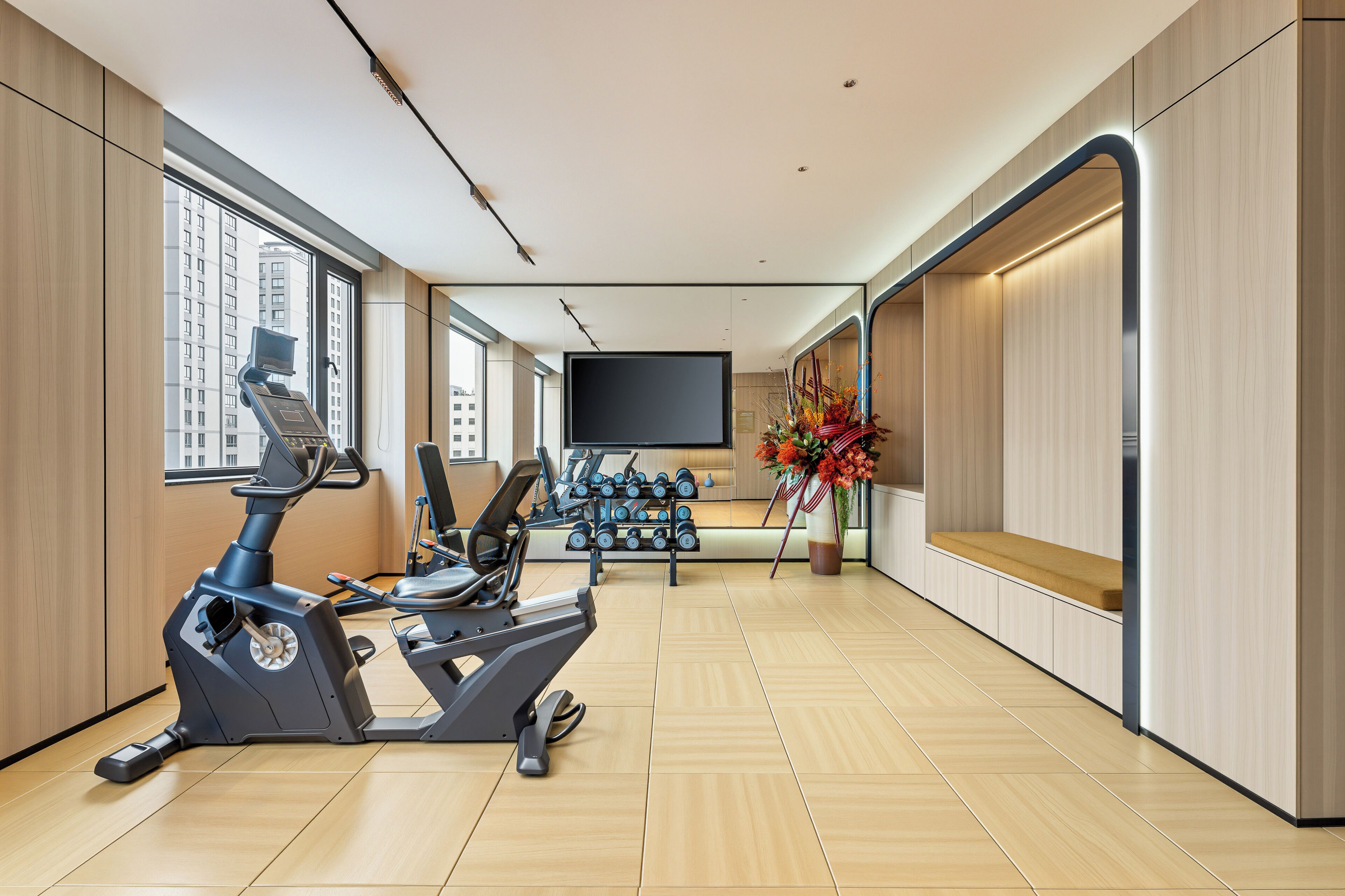 Un gimnasio moderno con equipo de ejercicio, un televisor y un amplio ventanal con vistas a la ciudad.