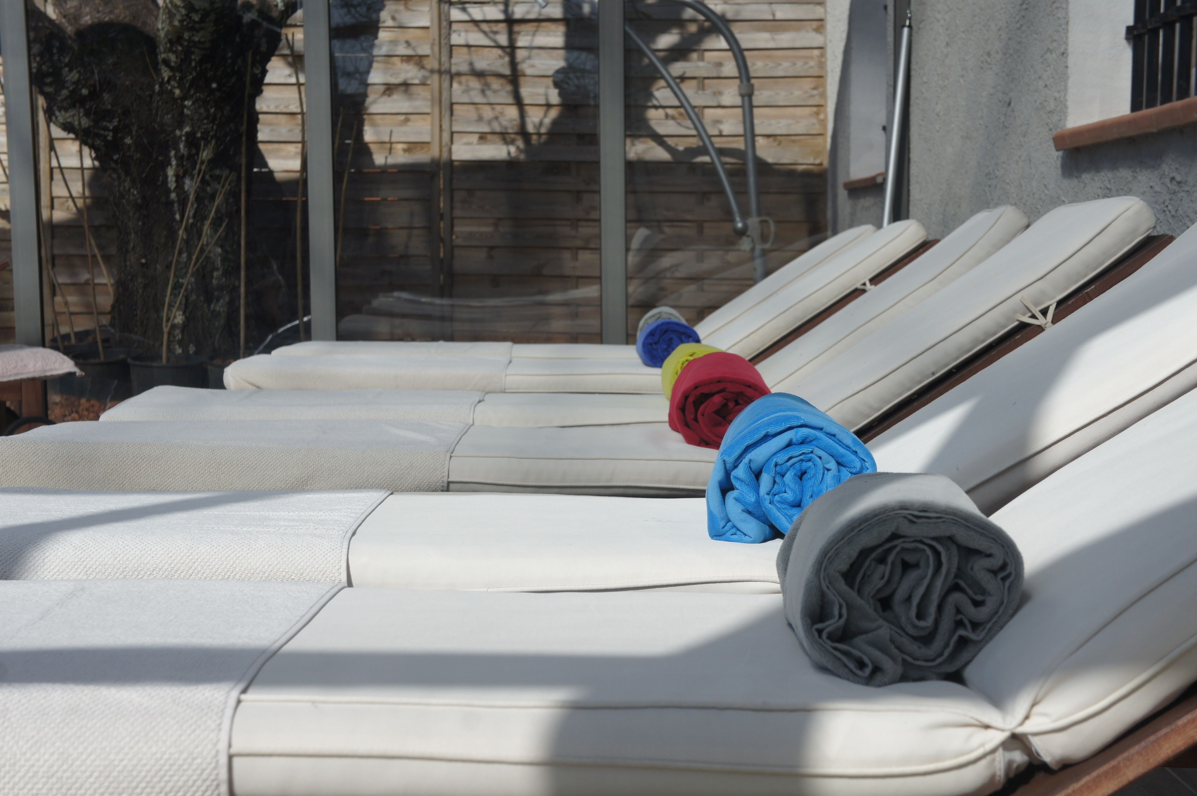 A row of white lounge chairs with towels and a rolled-up item on one of them.