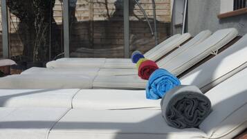 A row of white lounge chairs with towels and a rolled-up item on one of them.