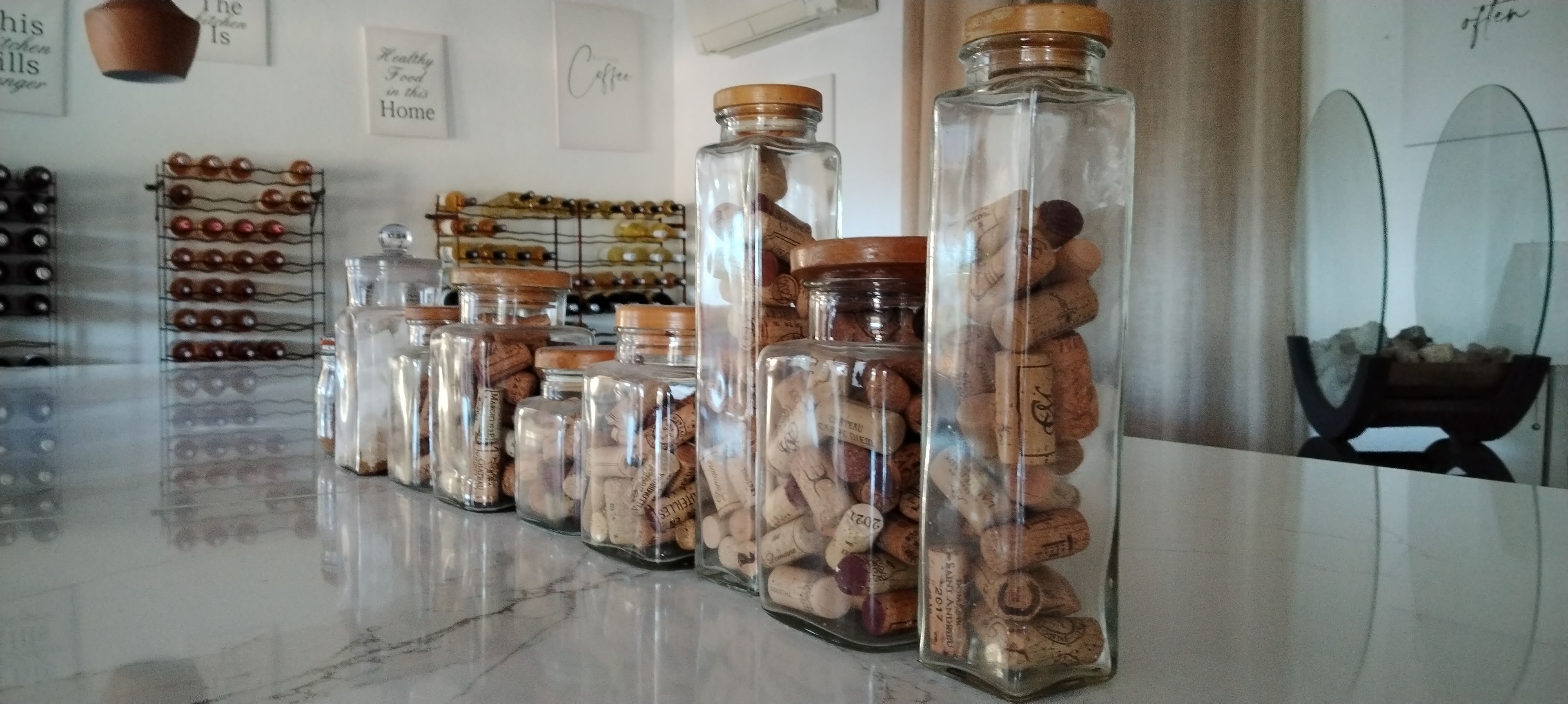 Una hilera de frascos de vidrio con tapones de corcho, algunos con tapas de madera, sobre una superficie reflectante.