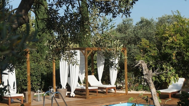 Een houten terras met een zwembad, witte zonnedaken en lounge fauteuils.