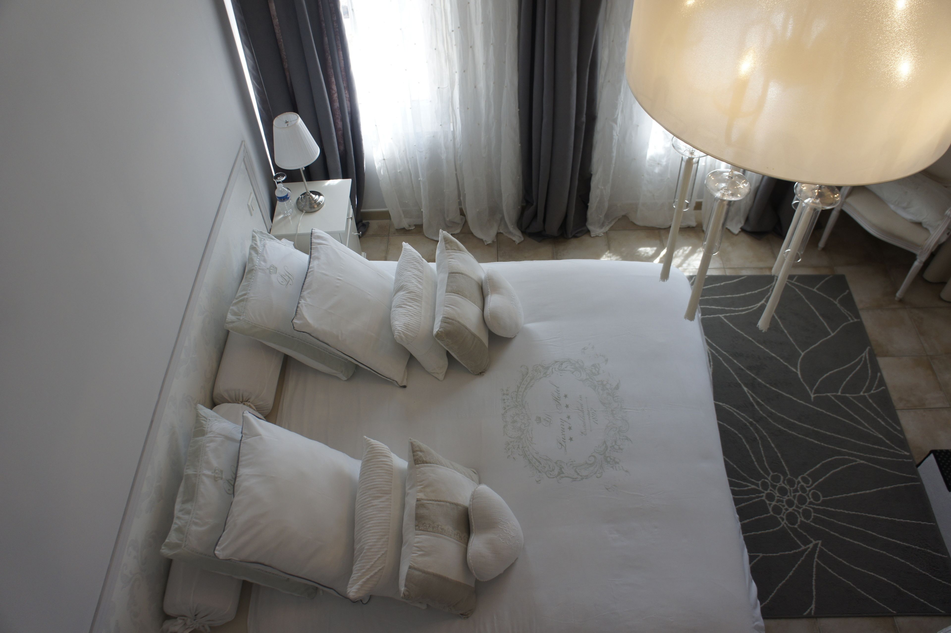 A neatly arranged hotel room with a large bed, multiple pillows, a bedside table with a lamp, and a decorative rug.