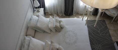 A neatly arranged hotel room with a large bed, multiple pillows, a bedside table with a lamp, and a decorative rug.