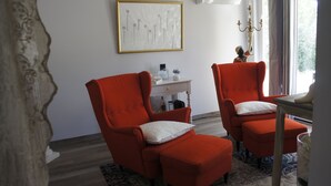Een kamer met twee rode fauteuils, een witte bijzettafeltje en een kunstwerk in een lijst aan de muur.