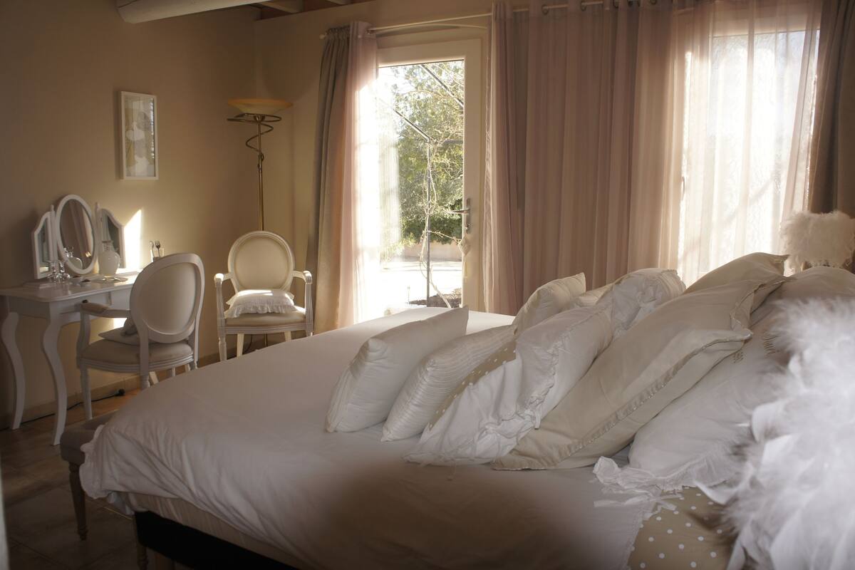 Une chambre à coucher avec un lit, une chaise, un bureau, un miroir et une fenêtre avec des rideaux.