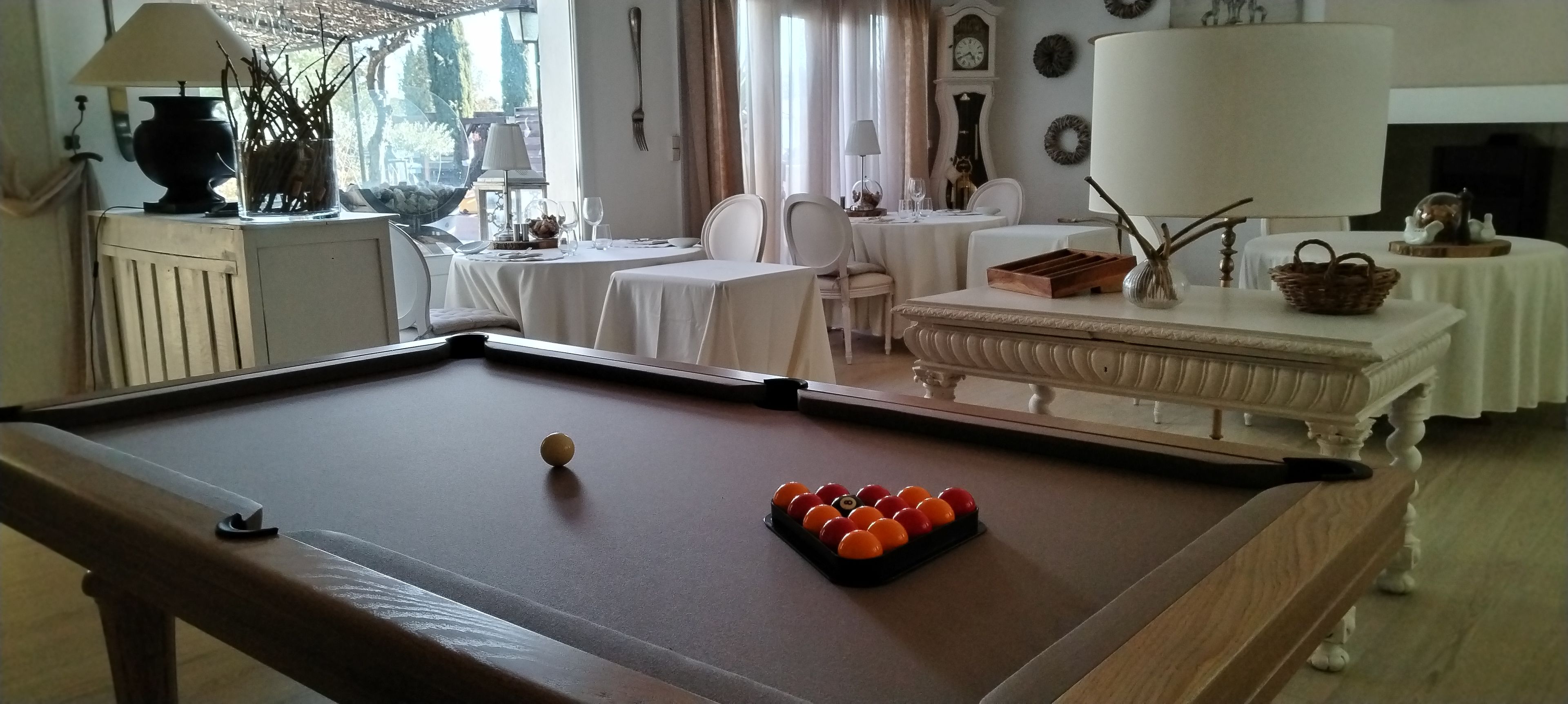 Ein Billardtisch mit Kugeln und Spielstöcken, ein Essbereich mit Tischen und Stühlen sowie ein Kamin.