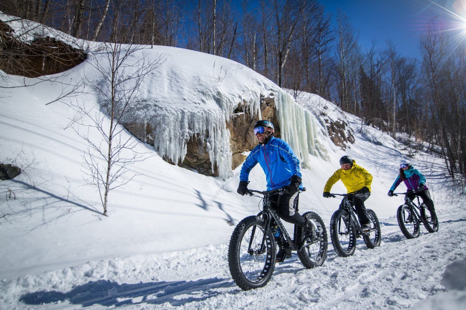 Three people on mountain bikes on a snowy slope with trees in the background.