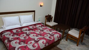 A hotel room with a bed, a nightstand, a chair, and a small table. - The Kings Kalindi Resort & Spa (Dhanaulti)