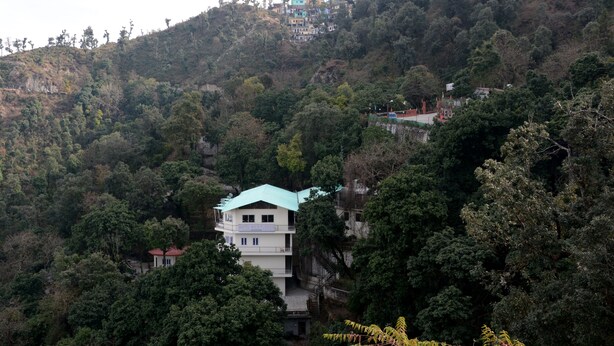 A multi-story building with a green roof nestled among dense forested hills. - The Kings Kalindi Resort & Spa (Dhanaulti)