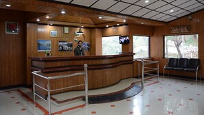 A reception area with a wooden reception desk, a television, framed pictures on the wall, and a seating area with chairs. - The Kings Kalindi Resort & Spa (Dhanaulti)