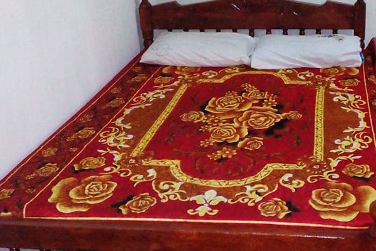 A bed with a red and gold patterned bedspread, a wooden headboard, and white pillows.