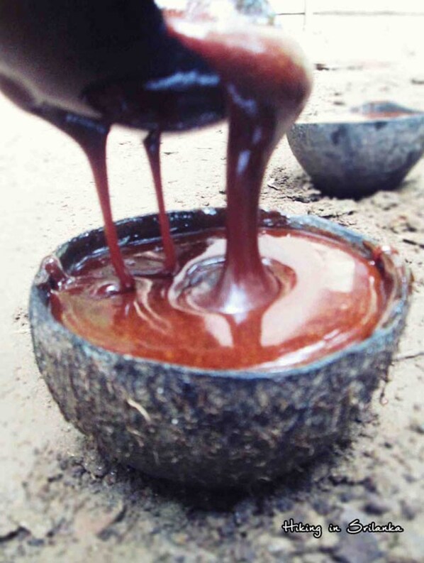 A hand pouring a thick, red liquid into a small, rustic bowl. - Meemure isabulana resort - Hostel (Udadumbara)