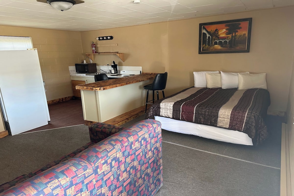 Ein kompaktes Hotelzimmer mit Bett, einer kleinen Küchenzeile, einem Esstisch und einem Sofa.