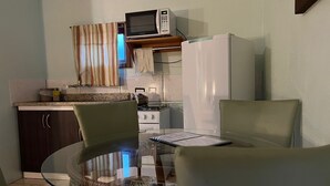 Une cuisine compacte équipée d’un four à micro-ondes, d’une cuisinière et d’un réfrigérateur. On y trouve une table en verre avec des chaises et un petit coin repas.