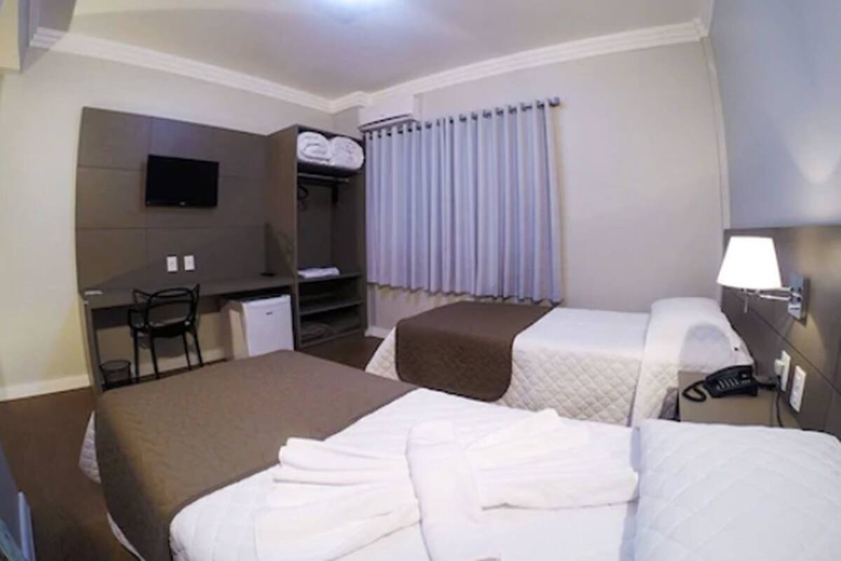 Habitación de hotel con dos camas, un escritorio, una silla, un televisor, un armario y una ventana con cortinas.