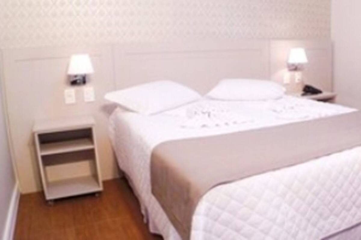 Una habitación de hotel ordenada con cama, mesitas de noche y un velador.
